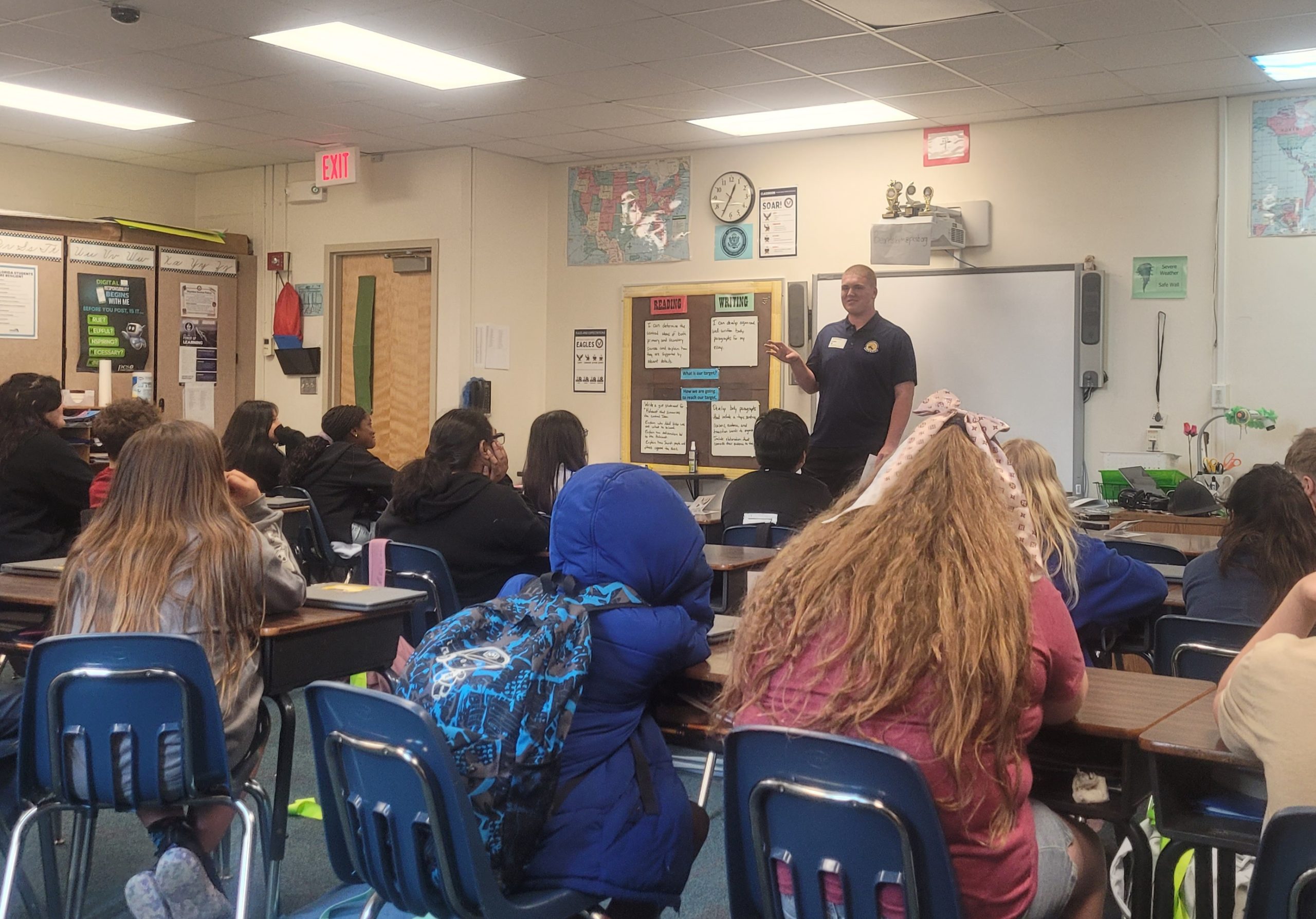 Classroom with students at desks facing front of room where a man is addressing class.